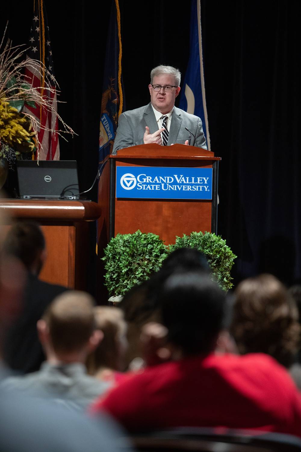 Man stands at a GVSU podium, talking and gesturing with his hands
